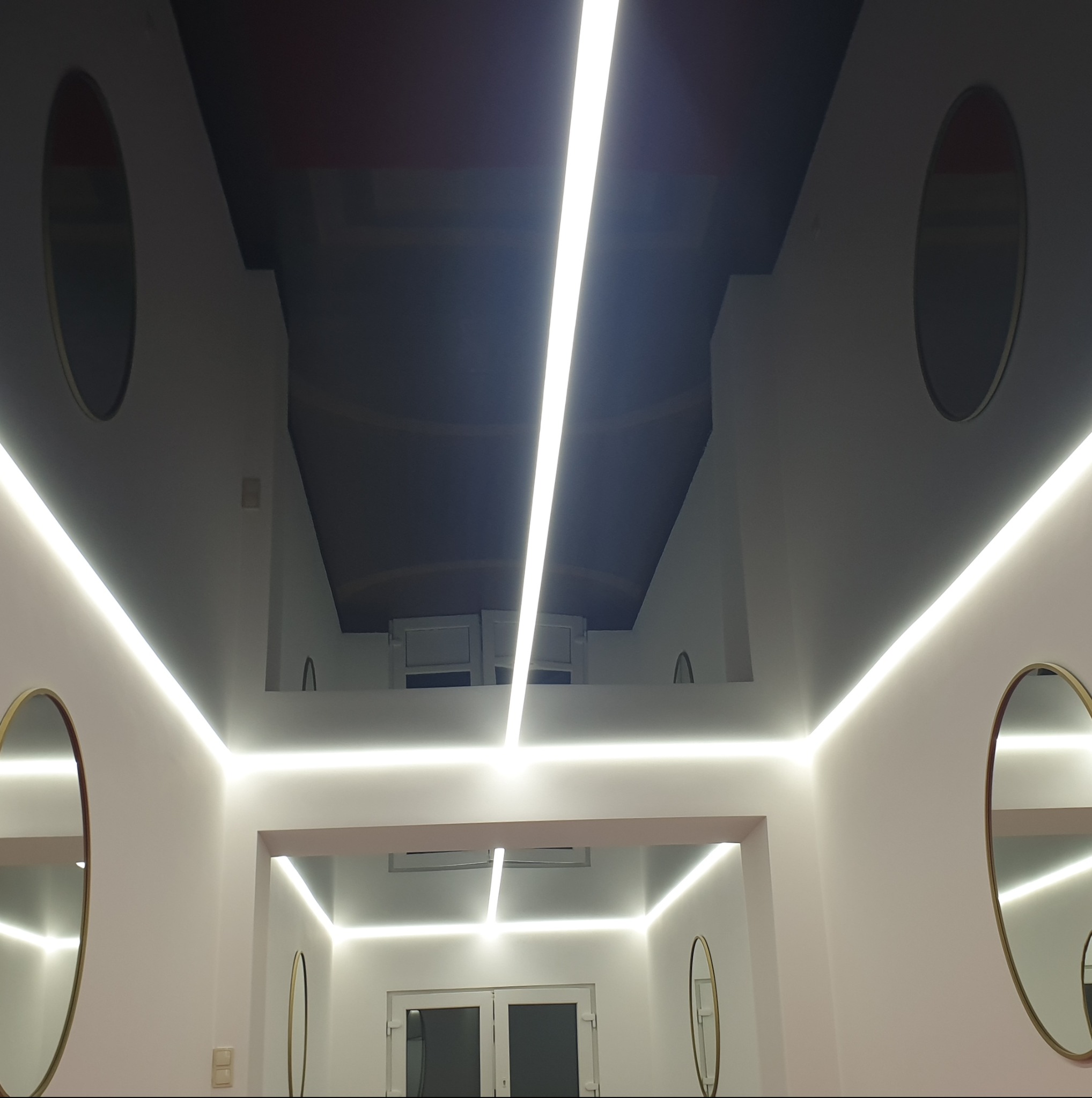 Nowoczesny sufit z podświetleniem LED tworzącym geometryczny wzór, uzupełniony owalnymi lustrami. Minimalistyczny design i jasne oświetlenie.