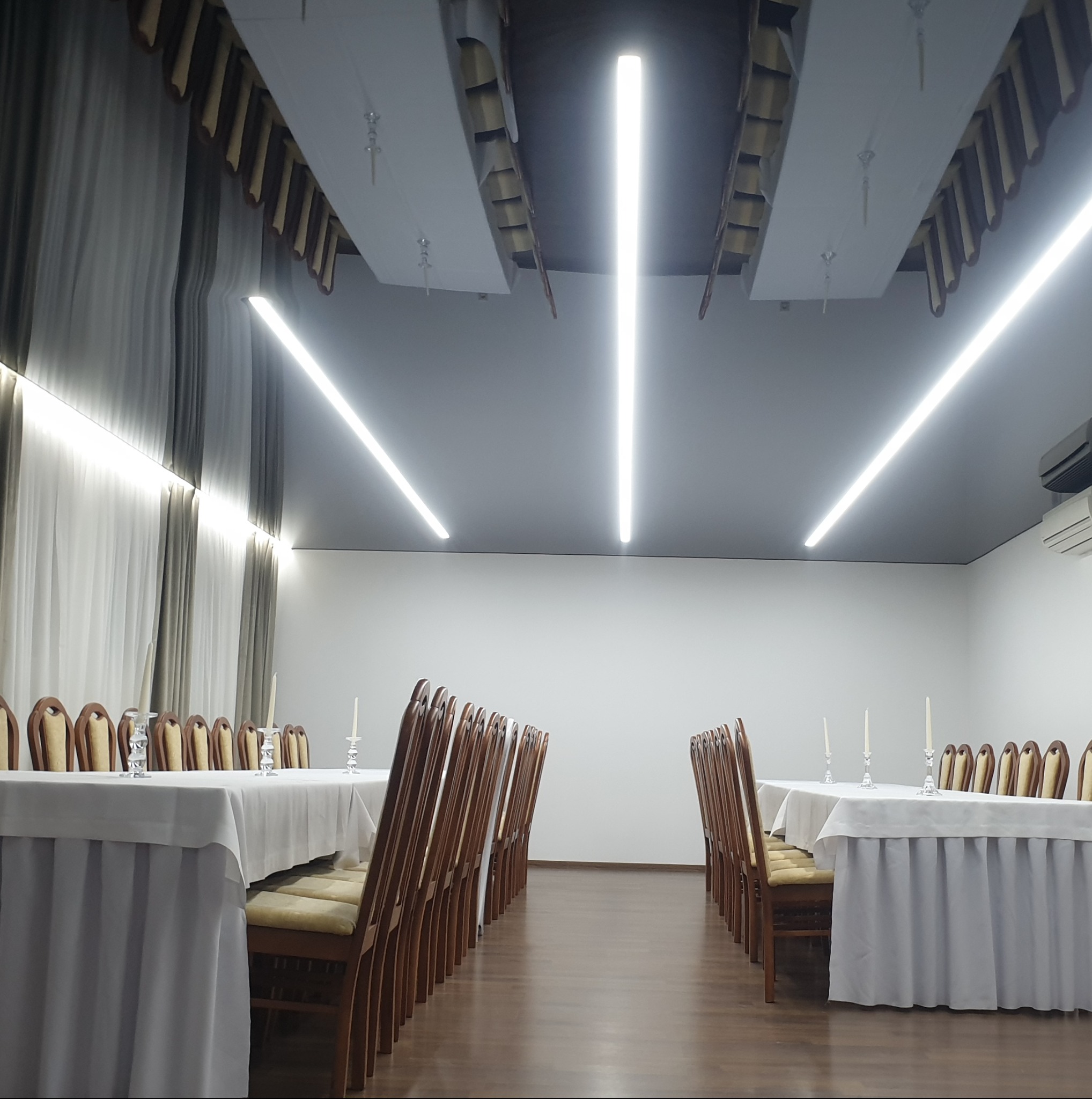 Sala bankietowa z oświetleniem LED i dekoracyjnym sufitem w Piasecznie. Widoczne stoły z krzesłami, gotowe na przyjęcie. Minimalistyczny design.