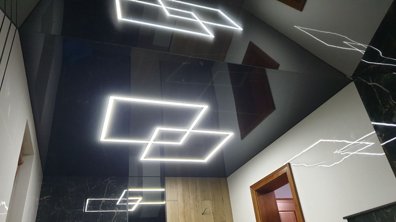 Błyszczący, czarny sufit napinany z geometrycznym oświetleniem LED w kształcie kwadratów, odbijający elementy wystroju wnętrza.