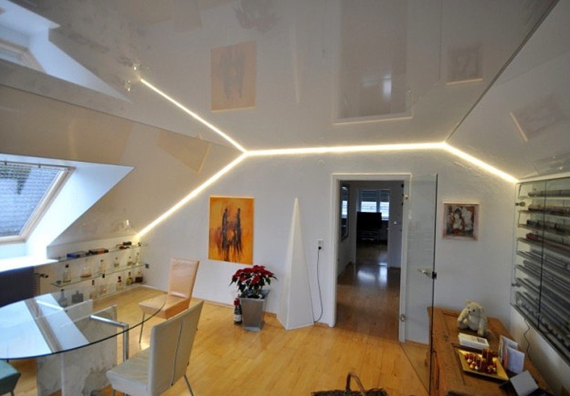 Błyszczący, biały sufit z oświetleniem LED wzdłuż krawędzi, pokój na poddaszu z oknem dachowym, szklany stół i drewniana podłoga.