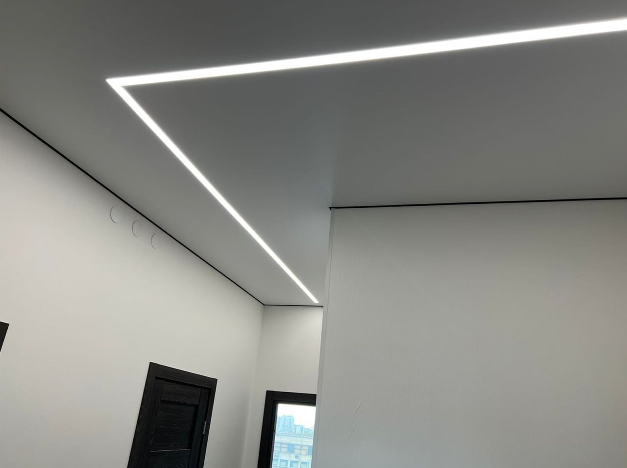 Biały sufit z napinanym, matowym wykończeniem i wbudowanym oświetleniem LED w kształcie prostokąta, czarne listwy wykończeniowe, minimalistyczny design.