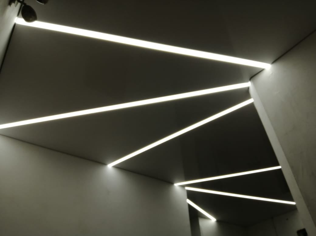 Nowoczesny, minimalistyczny sufit z liniowym oświetleniem LED w neutralnej tonacji, tworzącym geometryczny wzór na gładkiej powierzchni.