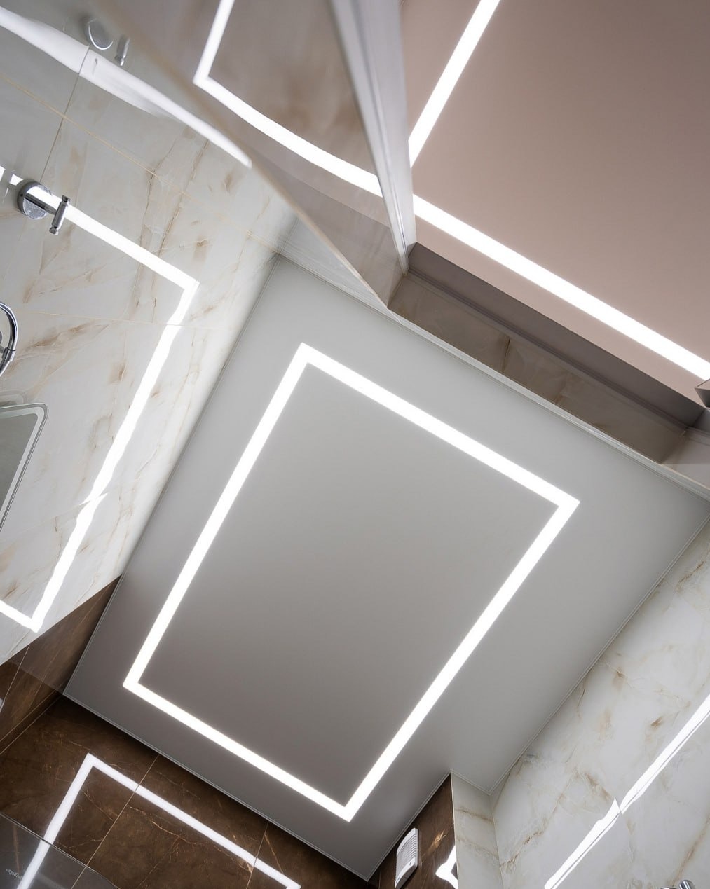 Biały sufit z oświetleniem LED w kształcie prostokąta, w łazience wykończonej marmurowymi płytkami w odcieniach brązu i beżu. Nowoczesny design i eleganckie wykończenie.