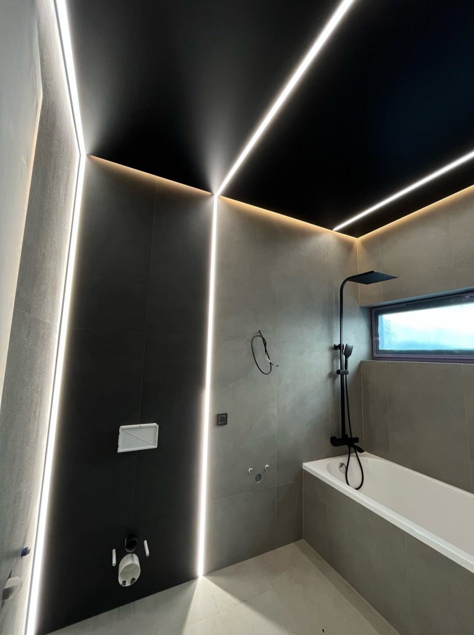 Nowoczesna łazienka z czarnym sufitem i liniowym oświetleniem LED wzdłuż ścian, podkreślającym minimalistyczny design i nową armaturę.