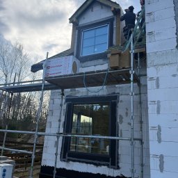 JR MONTER - Budowa domu z białych bloczków: pracownicy na rusztowaniu montują okna i ocieplenie Rockwool. Widok z dołu na surowy stan budynku.