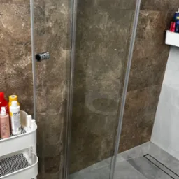 Wyczyszczona kabina prysznicowa w Pępowo, z widoczną armaturą i wózkiem z detergentami. Szklane drzwi bez smug, brązowe płytki i szara podłoga.