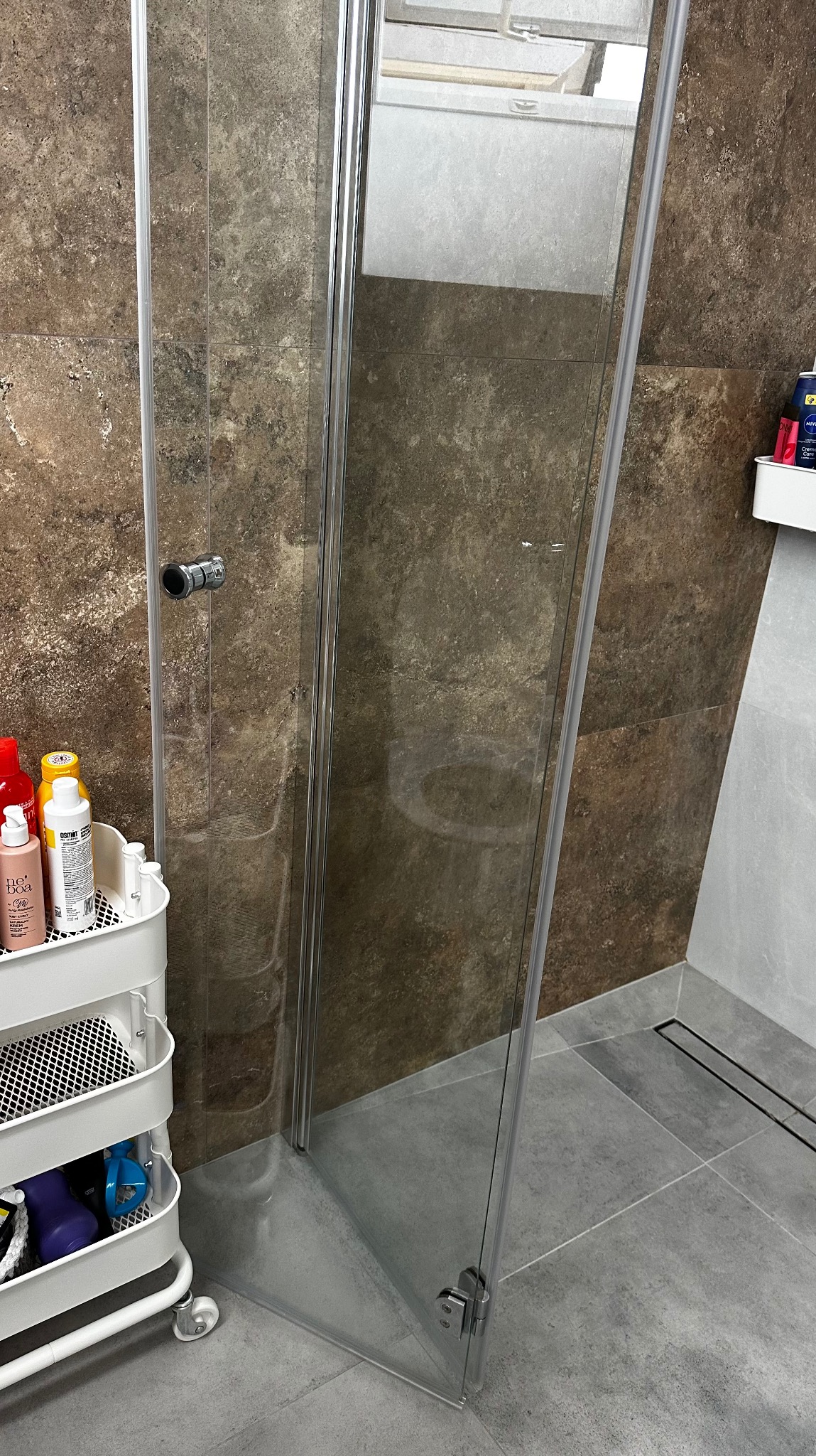 Wyczyszczona kabina prysznicowa w Pępowo, z widoczną armaturą i wózkiem z detergentami. Szklane drzwi bez smug, brązowe płytki i szara podłoga.