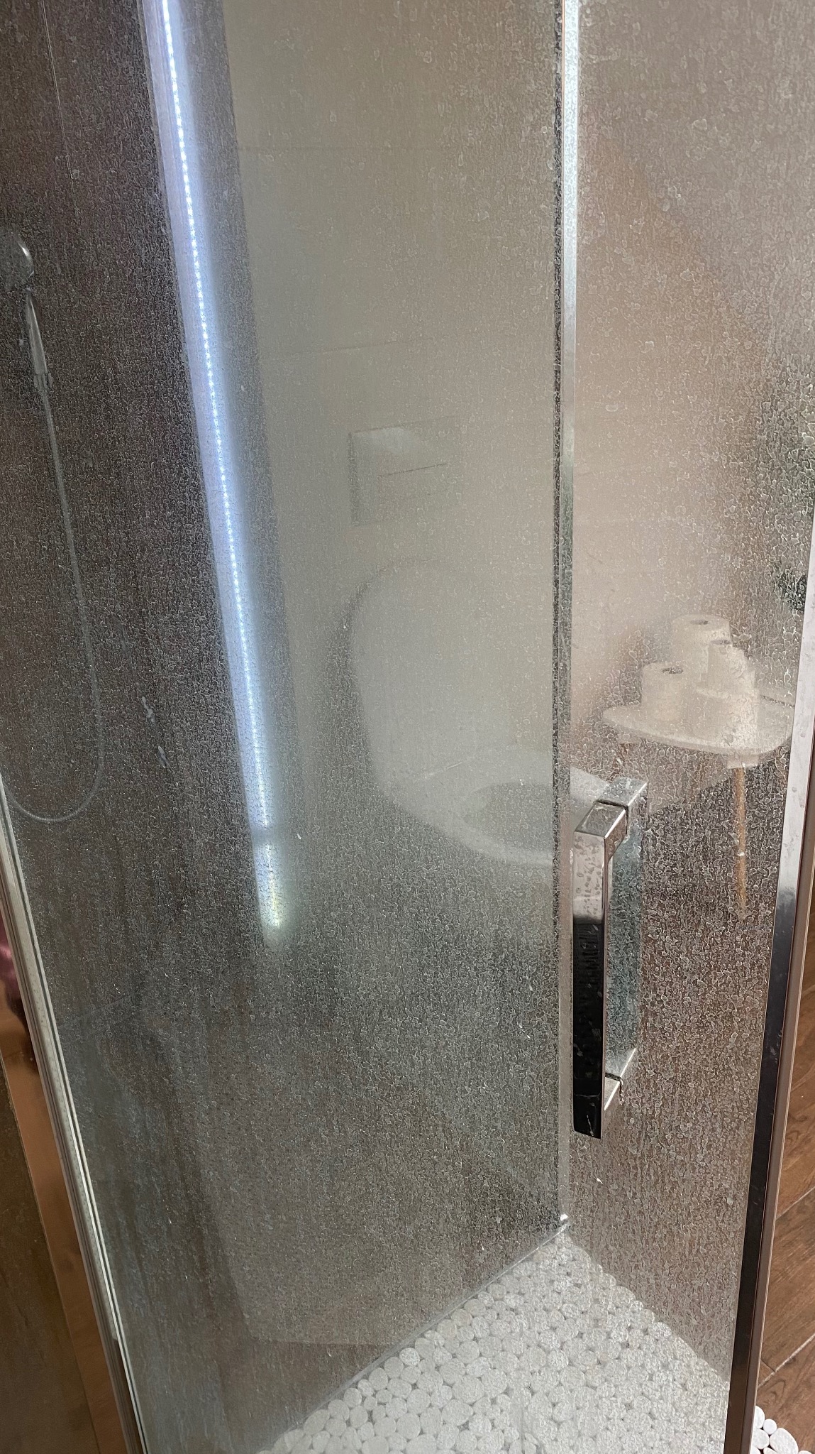 Zabrudzona kabina prysznicowa z widocznymi osadami na szklanych drzwiach i armaturze, ukazująca potrzebę dokładnego czyszczenia łazienki.