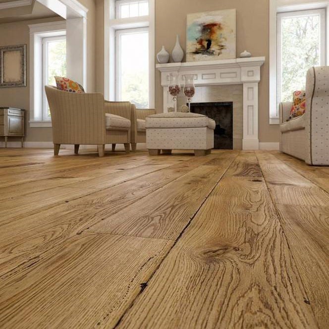 Jasna, drewniana podłoga z wyraźnym usłojeniem w salonie z kominkiem. Widoczne dwa fotele i pufa w tle. Na kominku dekoracje i kieliszki.