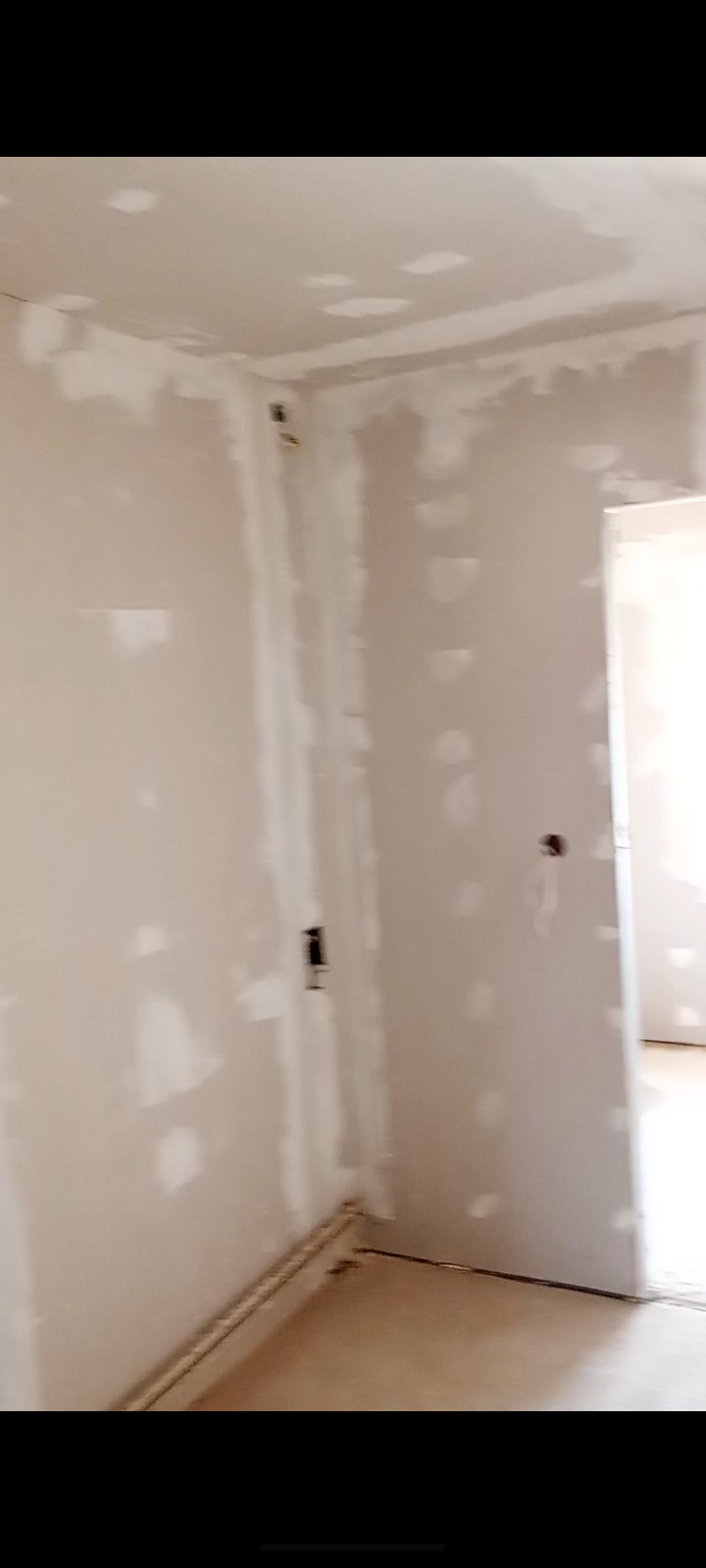 Pokój po szpachlowaniu ścian, widoczne ślady gładzi gipsowej, przygotowany do malowania. Fragment grzejnika przy podłodze. Otwór drzwiowy w tle.