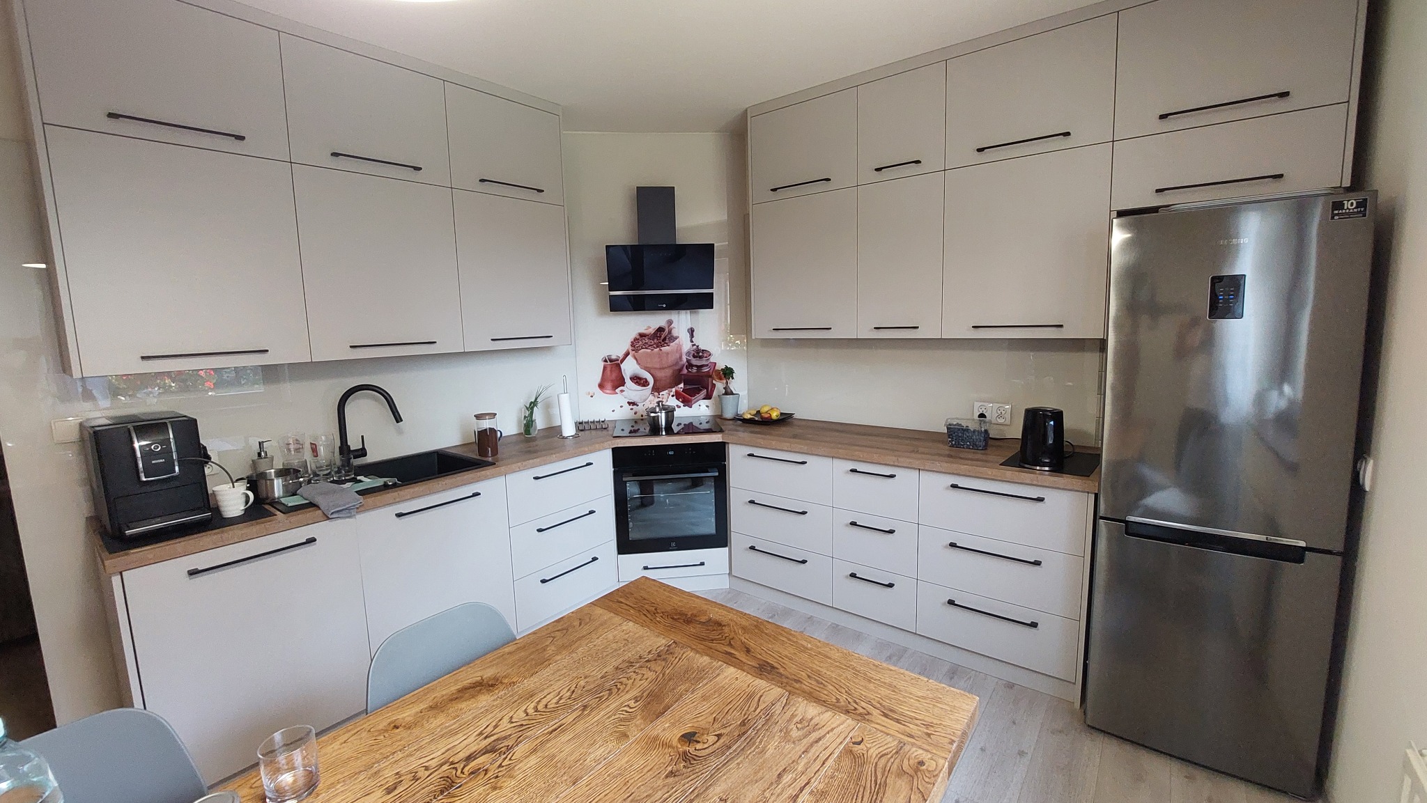 Jasna kuchnia z drewnianym blatem i czarnymi uchwytami, z zabudową od podłogi do sufitu, z widocznym stołem z litego drewna na pierwszym planie.