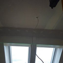 Regmal Romuald Muzika - Sufit z płyt karton-gips, widoczne dwa okna dachowe, szpachlowane łączenia, laser krzyżowy wyznacza poziom. Przewód elektryczny zwisa z sufitu.