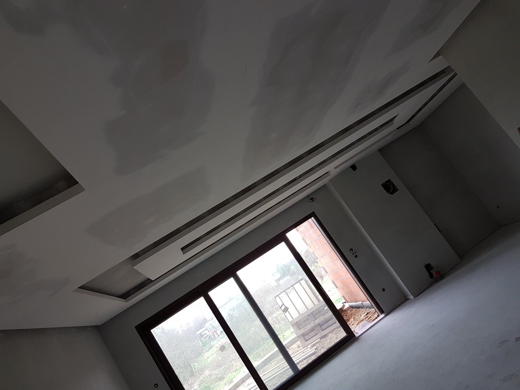 Sufit z płyt g-k z ozdobnymi elementami w Sycowie, po szpachlowaniu, przygotowany do malowania. Widok na okno i surowy stan wykończenia.