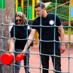 EUROPEJSKIE CENTRUM JAKOŚCI I PROMOCJI SPÓŁKA Z OGRANICZONĄ ODPOWIEDZIALNOŚCIĄ - Dwóch mężczyzn w granatowych koszulkach z logo, testuje sprawność zabawki na placu zabaw, sprawdzając certyfikację bezpieczeństwa.