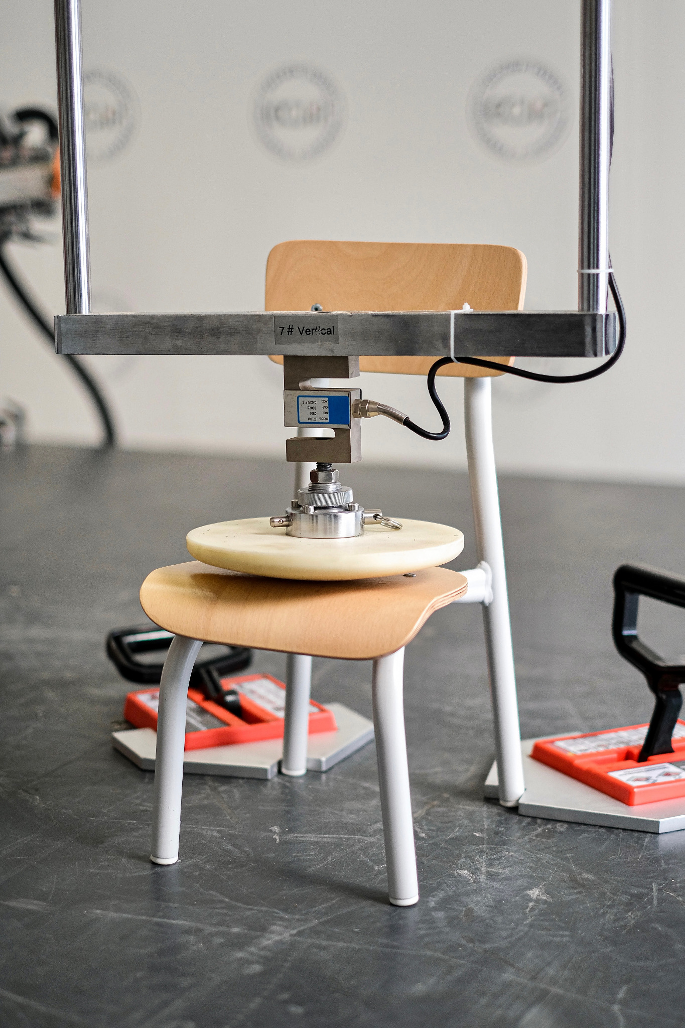 Test obciążeniowy krzesła biurowego przy użyciu specjalistycznej maszyny pomiarowej. Widoczne czujniki i elementy konstrukcyjne.