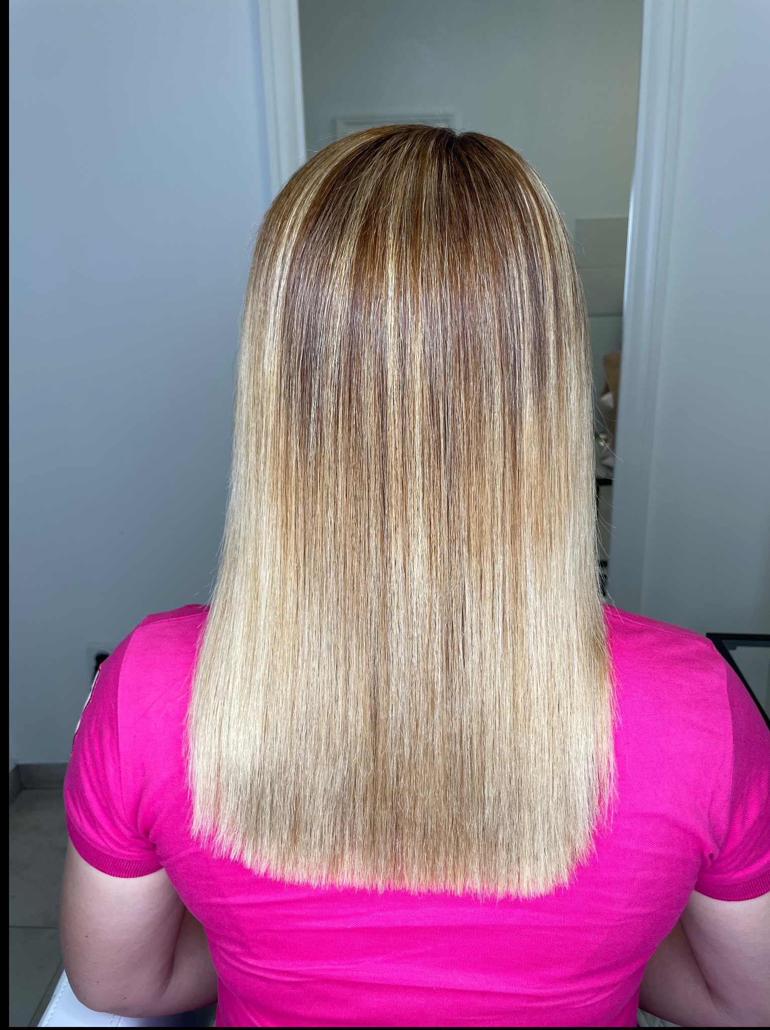 Tył głowy z prostymi, blond włosami z brązowymi pasemkami, po koloryzacji. Włosy sięgają do ramion, osoba ubrana w różową koszulkę polo.