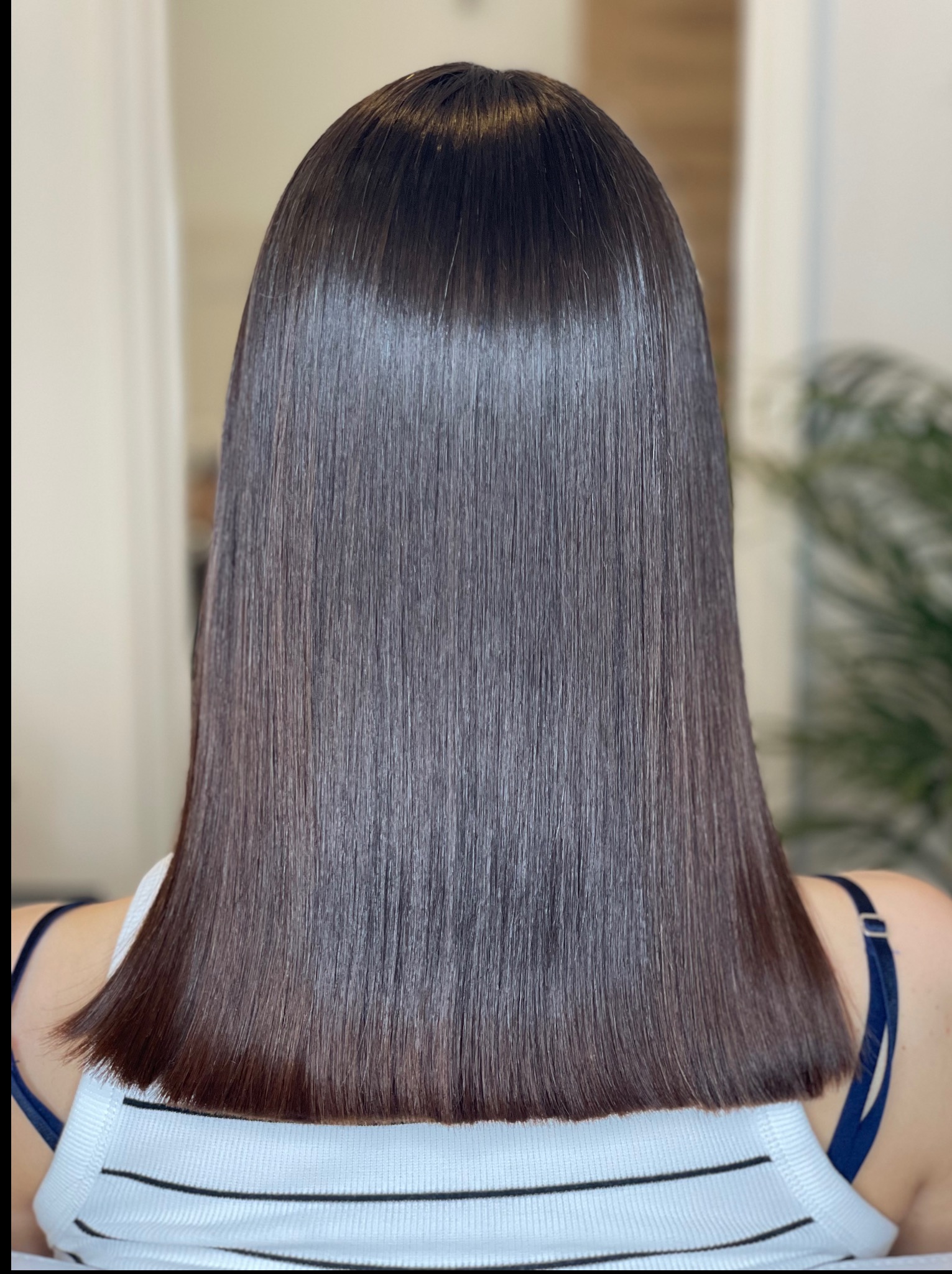Gładkie, ciemne włosy do ramion, po zabiegu prostowania keratynowego, widoczne od tyłu. Stylizacja z połyskiem, końcówki lekko podwinięte.