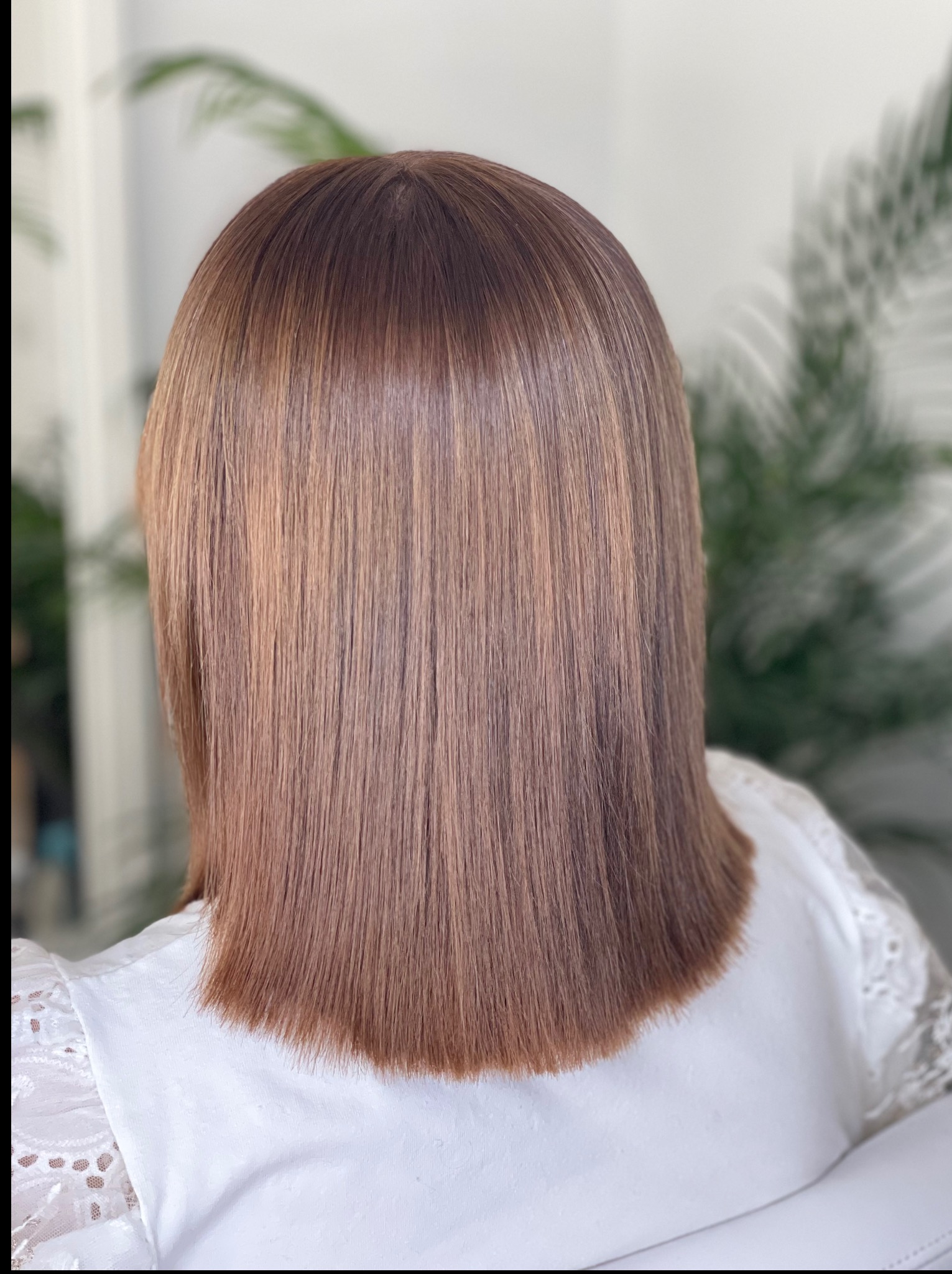 Włosy klientki po zabiegu koloryzacji i strzyżenia na prosto, widok z tyłu. Włosy w odcieniach brązu z refleksami, gładkie i lśniące.