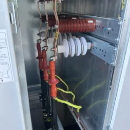 Rozdzielnica elektryczna z widocznymi elementami przyłączeniowymi, izolatorami i przewodami wewnątrz metalowej obudowy. Detal instalacji elektrycznej.