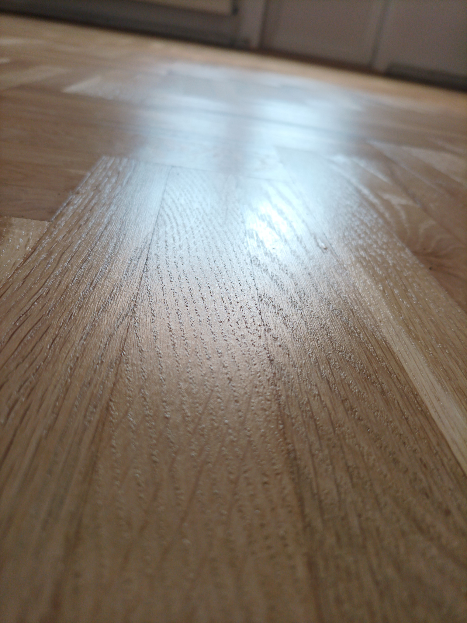 Błyszczący, drewniany parkiet z wyraźnym rysunkiem słojów, ułożony w regularny wzór. Widok z niskiej perspektywy, podkreślający strukturę i detale podłogi.