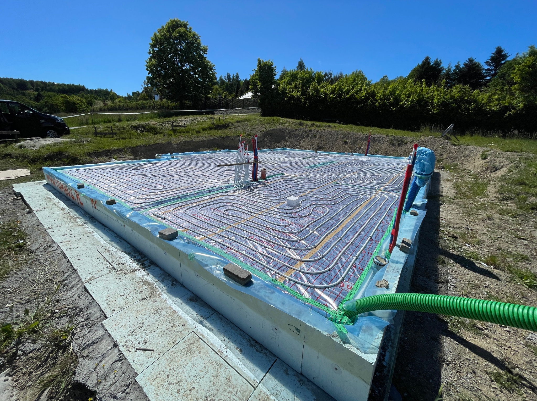 Fundament z izolacją i instalacją ogrzewania podłogowego na budowie domu. Widok na ułożone rury grzewcze i izolację termiczną w słoneczny dzień.
