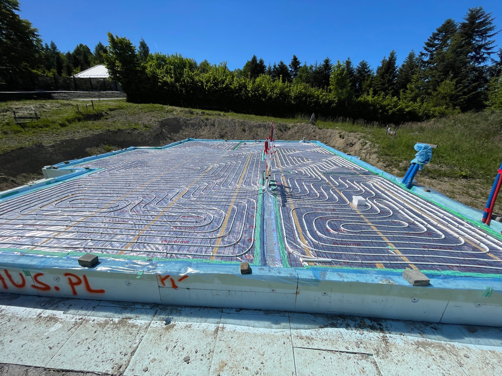 Instalacja ogrzewania podłogowego w fundamencie płyty budynku, widoczne rury grzewcze ułożone na izolacji, przygotowane do zalania betonem.