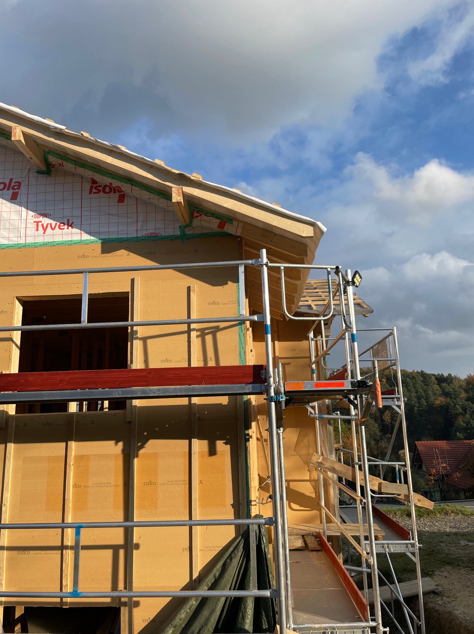 Budowa domu z drewnianą konstrukcją szkieletową w trakcie montażu, widoczne rusztowanie, izolacja Tyvek i STEICO.