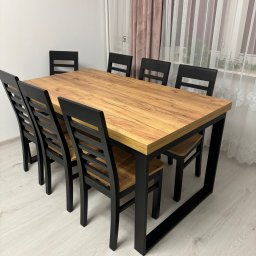 IDEAL FORM Dariusz Kuś - Stół z blatem imitującym drewno i czarnymi nogami oraz sześć krzeseł w pokoju z zasłonami. Zestaw mebli do jadalni.