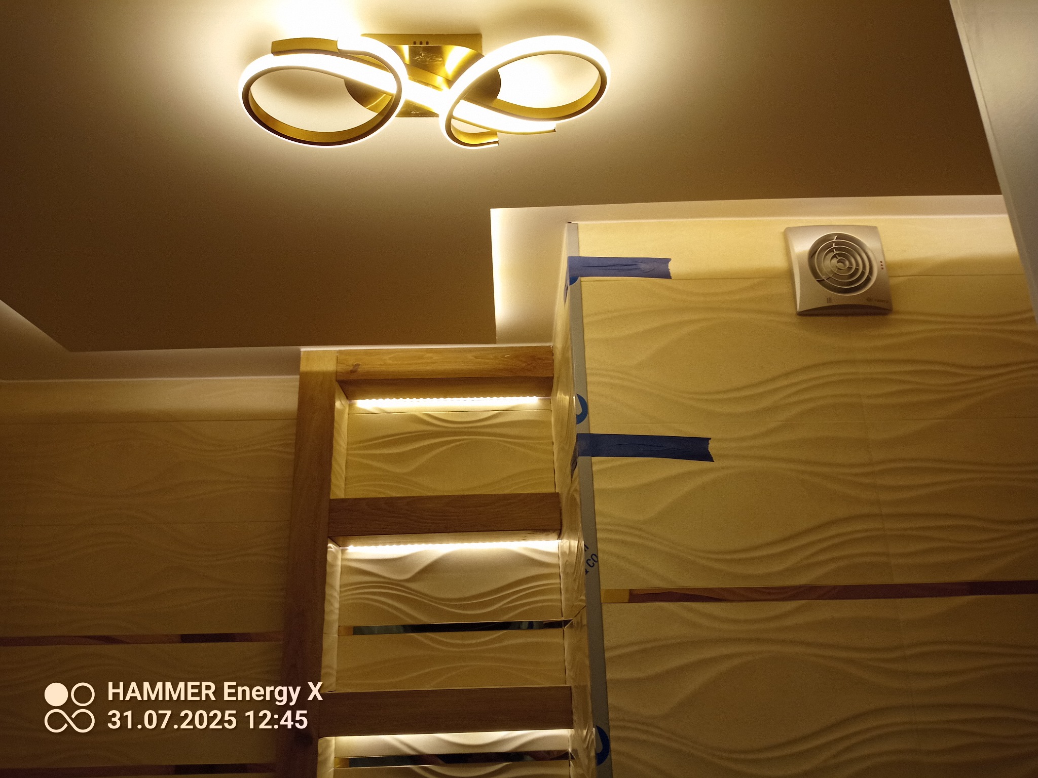 Nowoczesna łazienka w trakcie wykończenia: teksturowane panele ścienne, oświetlenie LED i wentylator. Fragment montażu z użyciem taśmy maskującej.