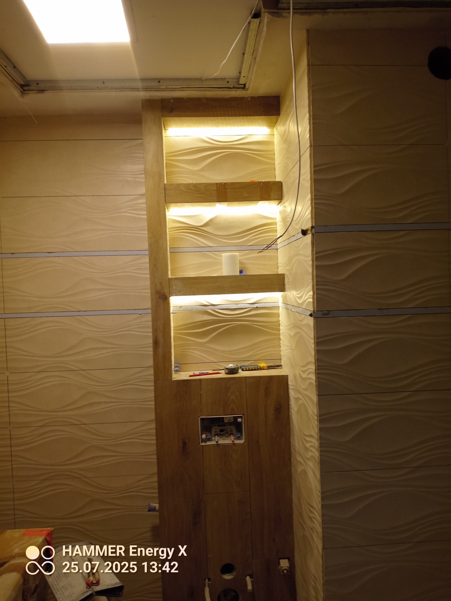 Montaż płytek 3D w łazience z podświetlaną wnęką. Widoczne narzędzia i elementy instalacji. Etap prac wykończeniowych z użyciem płytek o falistej strukturze.