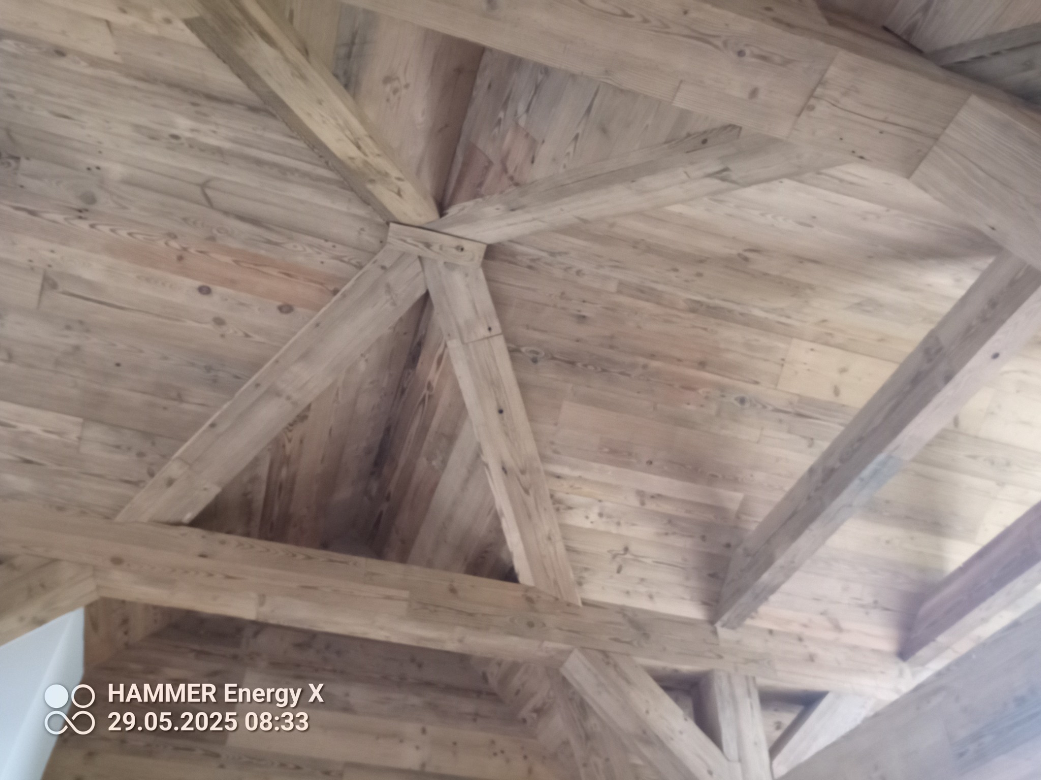 Drewniany sufit z widocznymi belkami stropowymi, wykończony w jasnym odcieniu drewna. Charakterystyczny układ belek tworzy geometryczny wzór.