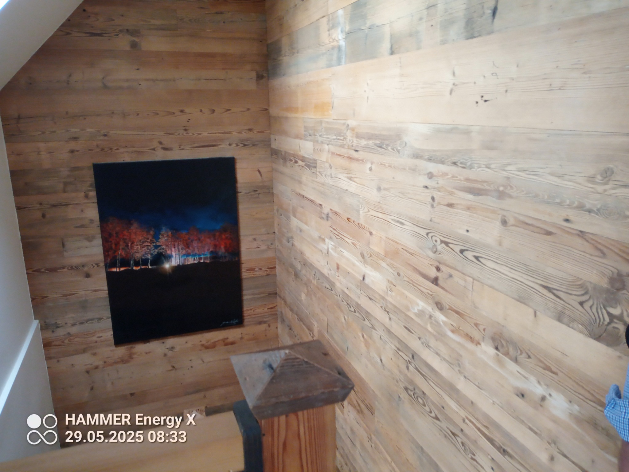 Drewniana boazeria na ścianach w rogu pomieszczenia, z obrazem na ścianie po lewej stronie. Widoczny fragment schodów i drewniany słupek.