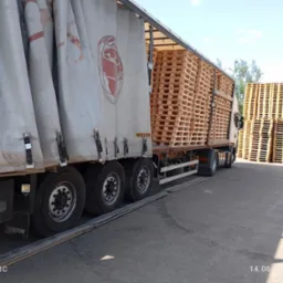 Ciężarówka marki Wielton z naczepą, załadowana paletami, zaparkowana na placu. Widoczne panele słoneczne w tle. Transport ciężarowy.