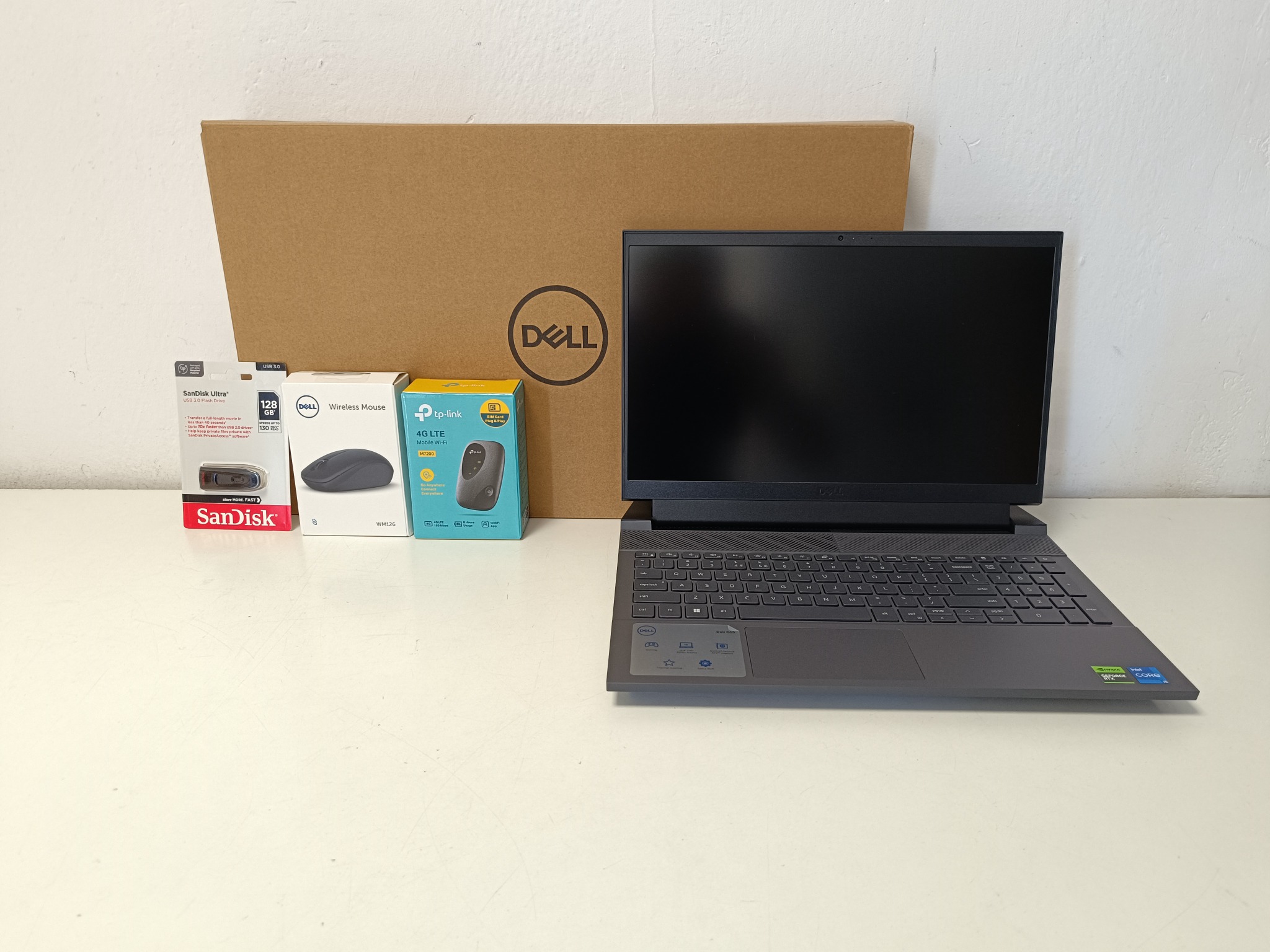 Nowy laptop Dell z akcesoriami: mysz bezprzewodowa, modem 4G LTE, pendrive SanDisk 128GB, pudełko Dell w tle. Kompletny zestaw komputerowy na białym tle.