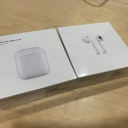 MKS Polska Rusinek Spółka Jawna - Dwa pudełka AirPods: z lewej etui ładujące, z prawej słuchawki. Nowe, białe, leżą na blacie. Widoczne napisy i grafiki Apple na opakowaniach.