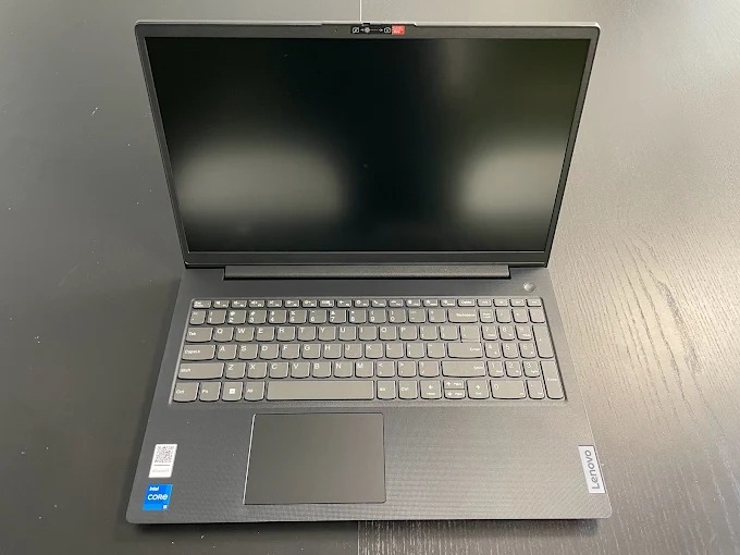 Otwarty laptop Lenovo z czarnym ekranem i szarą klawiaturą na ciemnym blacie. Widoczny touchpad, naklejka Intel Core i logo Lenovo. Górny widok.