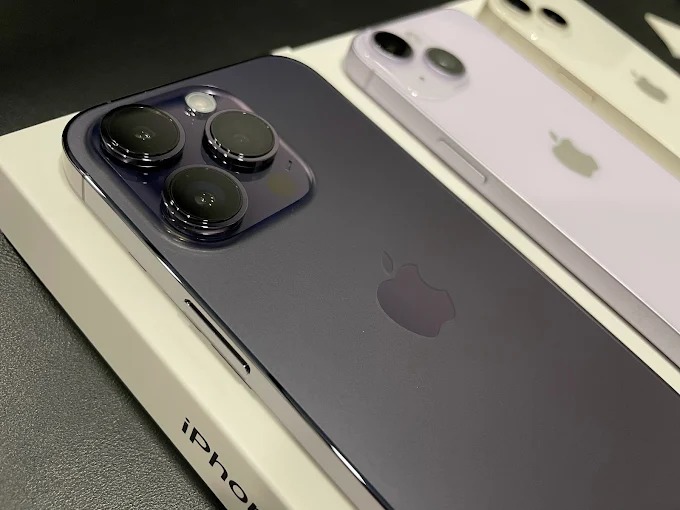 Układ trzech smartfonów iPhone: ciemnofioletowy z trzema obiektywami, fioletowy i biały. Widok z tyłu, logo Apple, na pudełku. Precyzyjne detale obudowy.