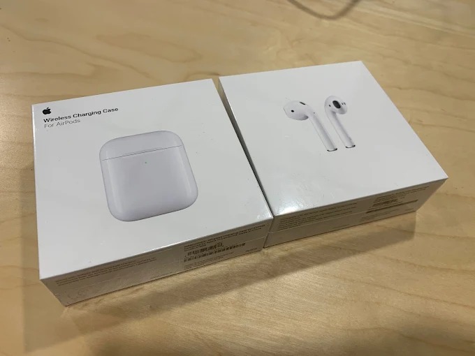 Dwa pudełka AirPods: z lewej etui ładujące, z prawej słuchawki. Nowe, białe, leżą na blacie. Widoczne napisy i grafiki Apple na opakowaniach.