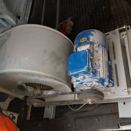 MEGAZORD - Wentylator przemysłowy z silnikiem elektrycznym, połączone paskiem klinowym, zamontowane na metalowej konstrukcji wewnątrz pojazdu serwisowego. Widoczne ślady użytkowania.