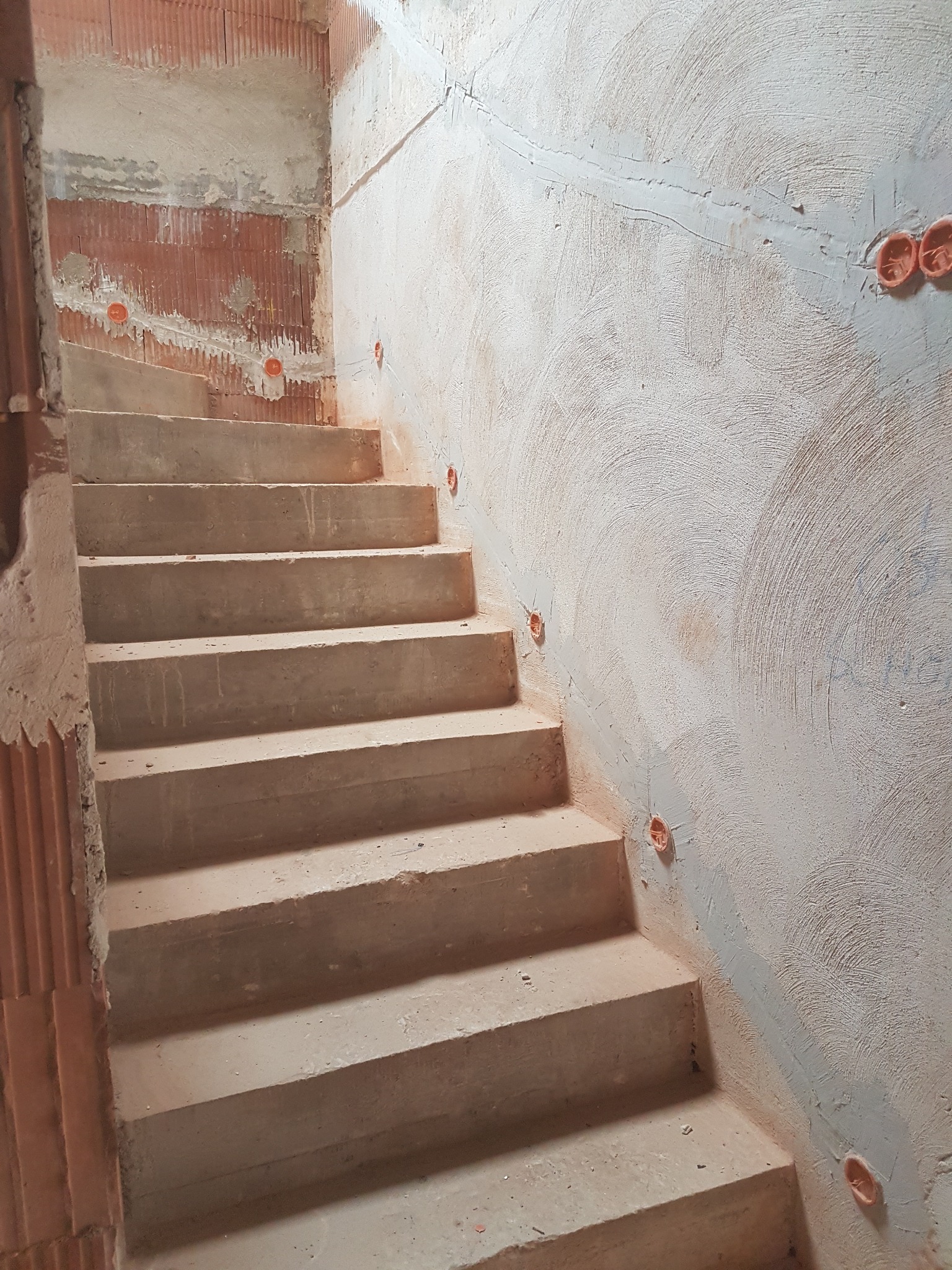 Betonowe schody w surowym stanie z widocznymi puszkami elektrycznymi w ścianie, przygotowane do dalszych prac wykończeniowych. Widoczne ślady po instalacji elektrycznej.