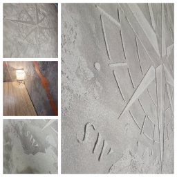 Wykończenia wnętrz - Dekoracyjna ściana z szarego betonu architektonicznego z motywem róży wiatrów, fragment oświetlonego blatu i lampy. Unikalna faktura i wzór.