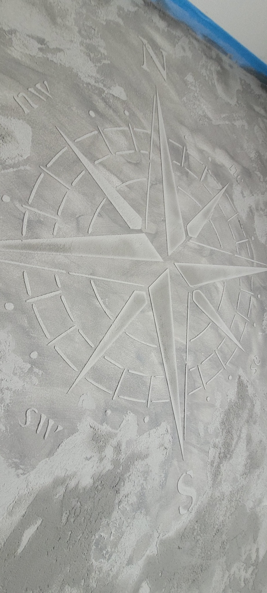 Dekoracyjna gładź na ścianie z motywem róży wiatrów, wykończona w odcieniach szarości. Efektowna tekstura i precyzyjne wykonanie detali.