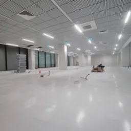 Wnętrze biurowe w trakcie montażu oświetlenia: widoczny sufit podwieszany z rastrem, lampy liniowe, kable i gniazda podłogowe. Stan surowy, przygotowanie do prac wykończeniowych.