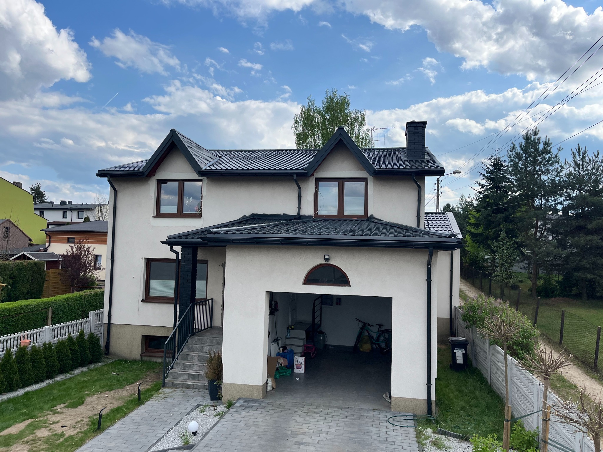 Dom z pomalowaną elewacją i dachem z czarnej dachówki, widok z zewnątrz w słoneczny dzień. Widoczny komin i rynna.