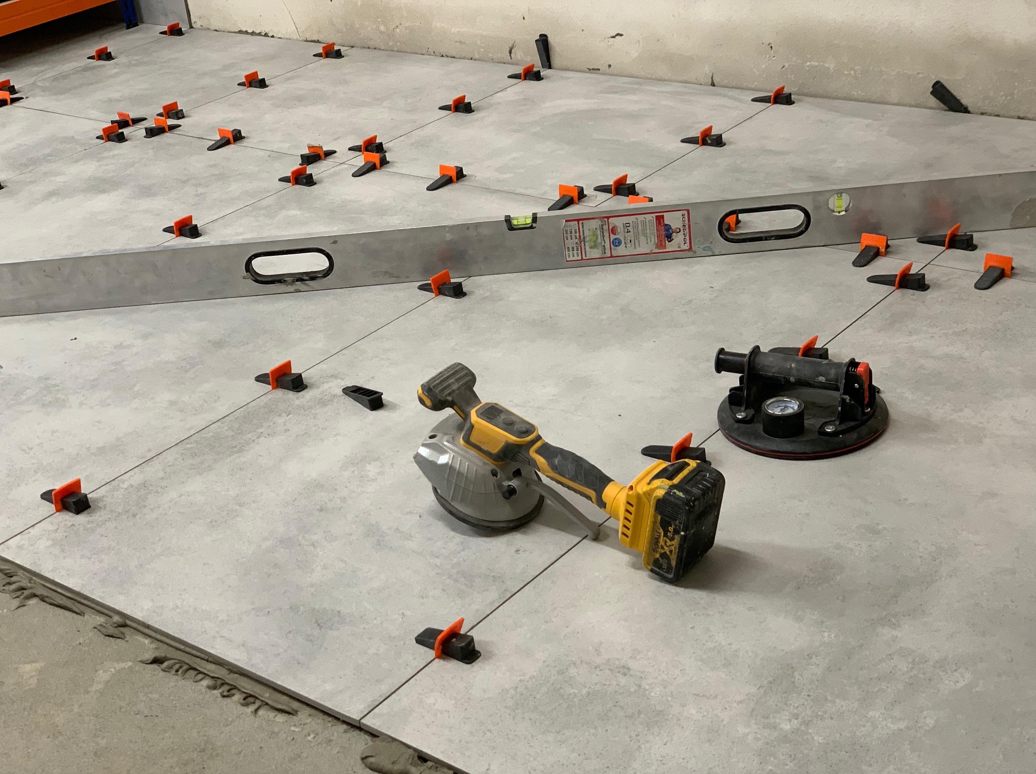 Układanie płytek podłogowych z użyciem poziomicy i przyssawek w Białymstoku. Widoczne systemy poziomowania płytek i narzędzia glazurnicze.