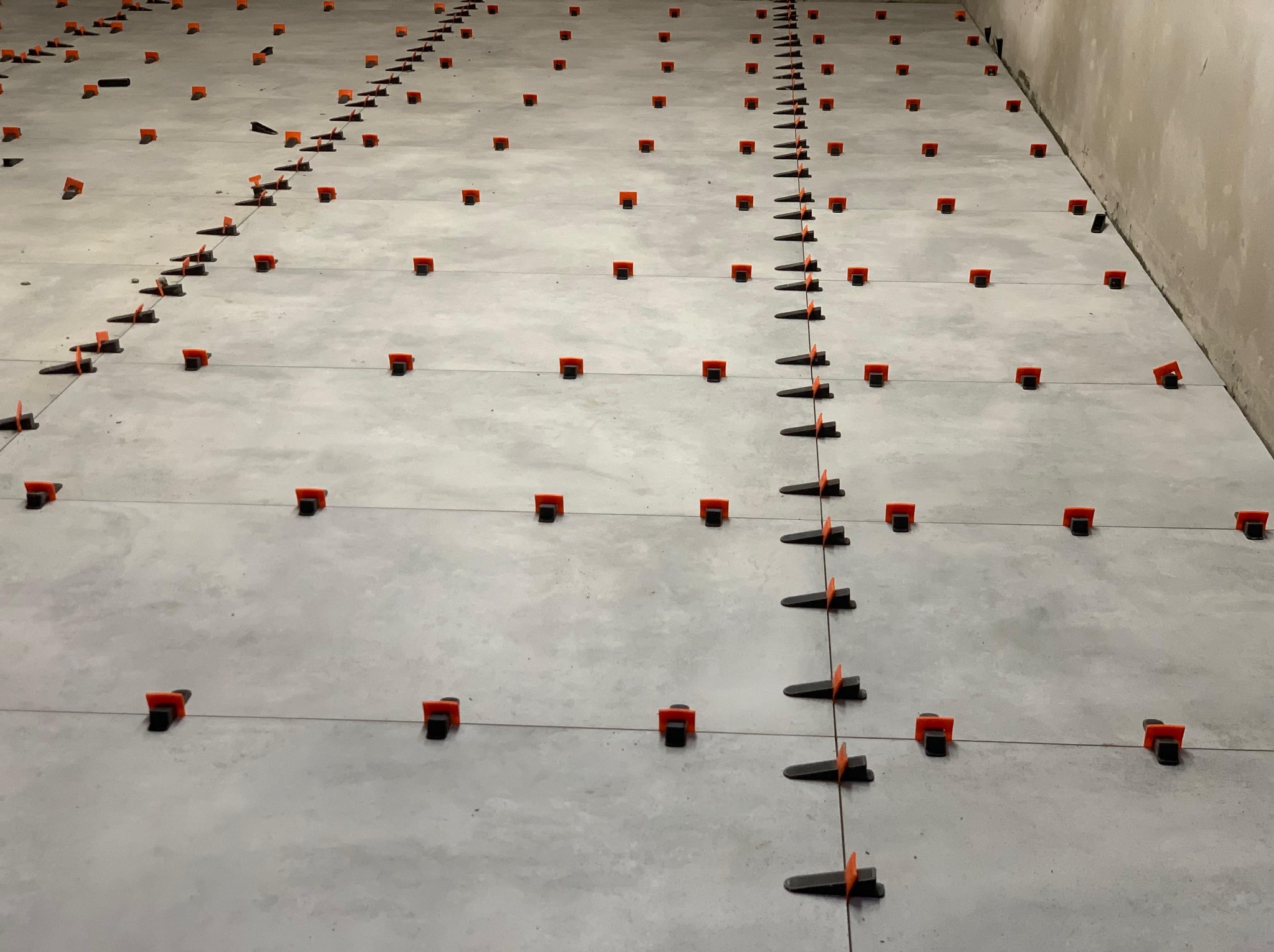 Ułożone szare płytki podłogowe z pomarańczowymi klipsami poziomującymi i czarnymi klinami, widok z góry, świeżo po ułożeniu.