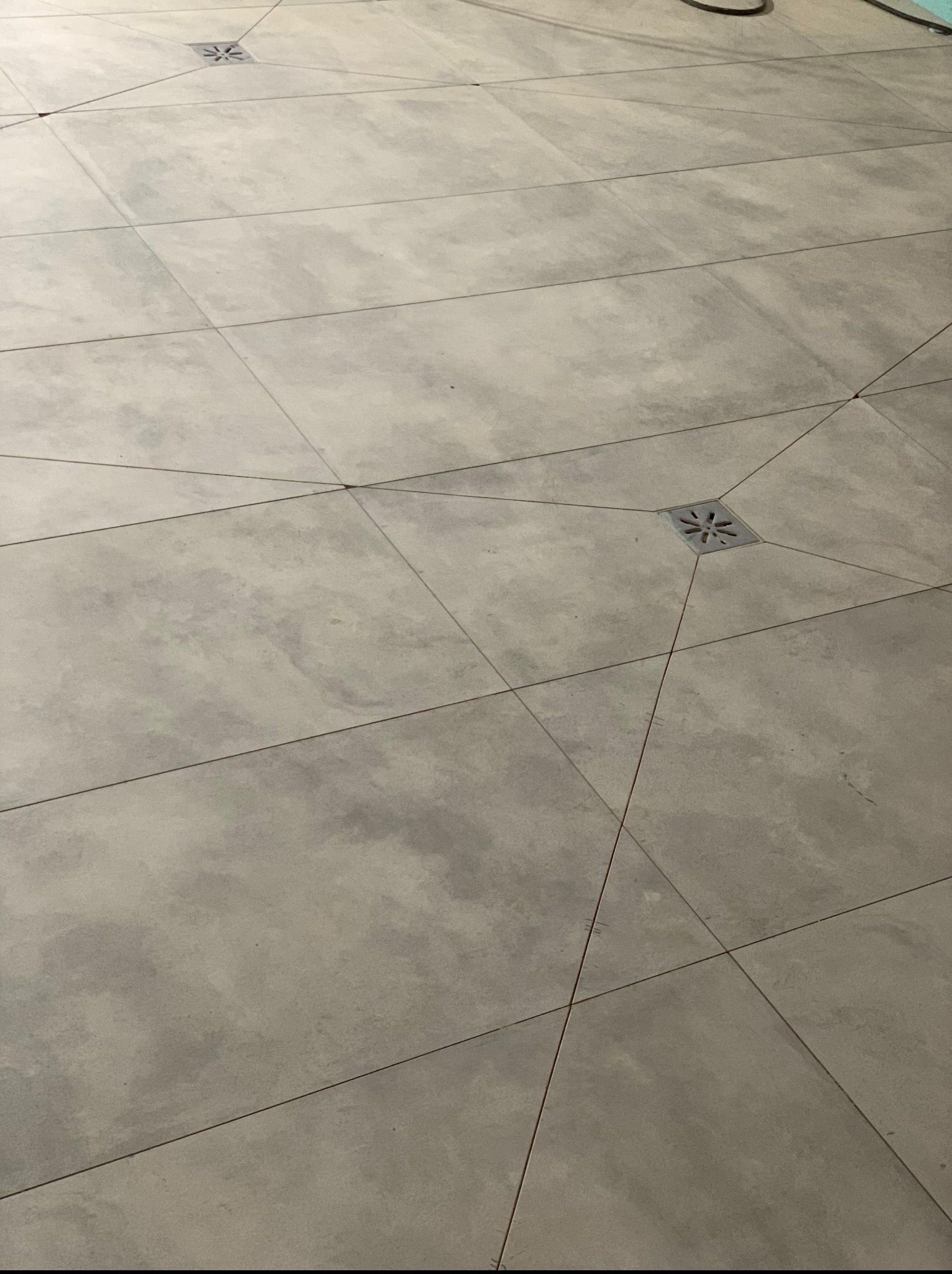 Ułożone szare płytki podłogowe z odpływem liniowym w rogu, widok z góry. Minimalistyczny wzór, równo ułożone fugi, stonowana kolorystyka.