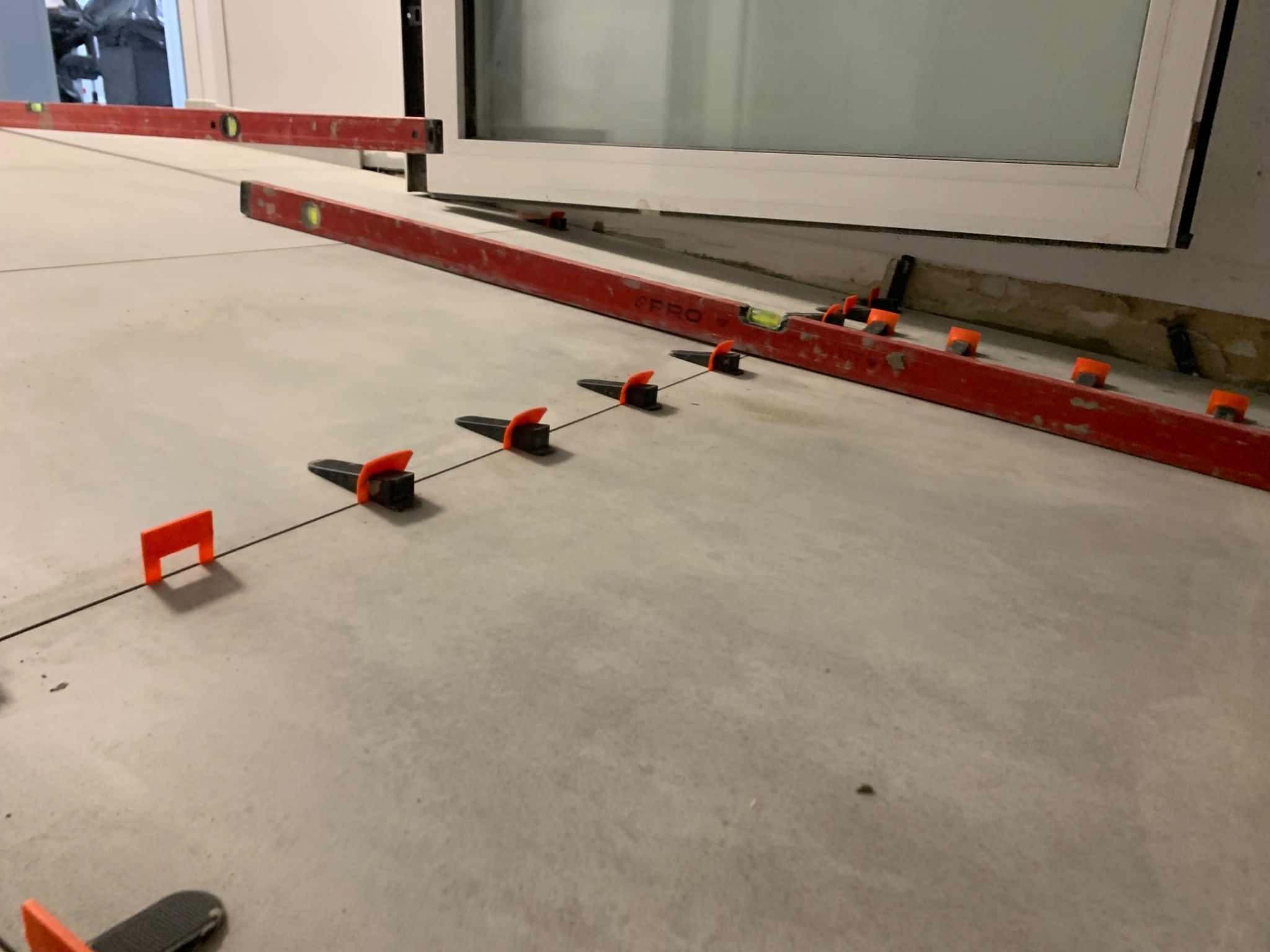 Poziomice i klipsy do wyrównywania płytek na podłodze, blisko okna. Etap prac wykończeniowych, widok z niskiej perspektywy.