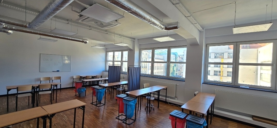 Jasne biuro po odświeżeniu: białe ściany, parkiet, widok z okna na miasto. Minimalistyczne meble i elementy wentylacji pod sufitem.