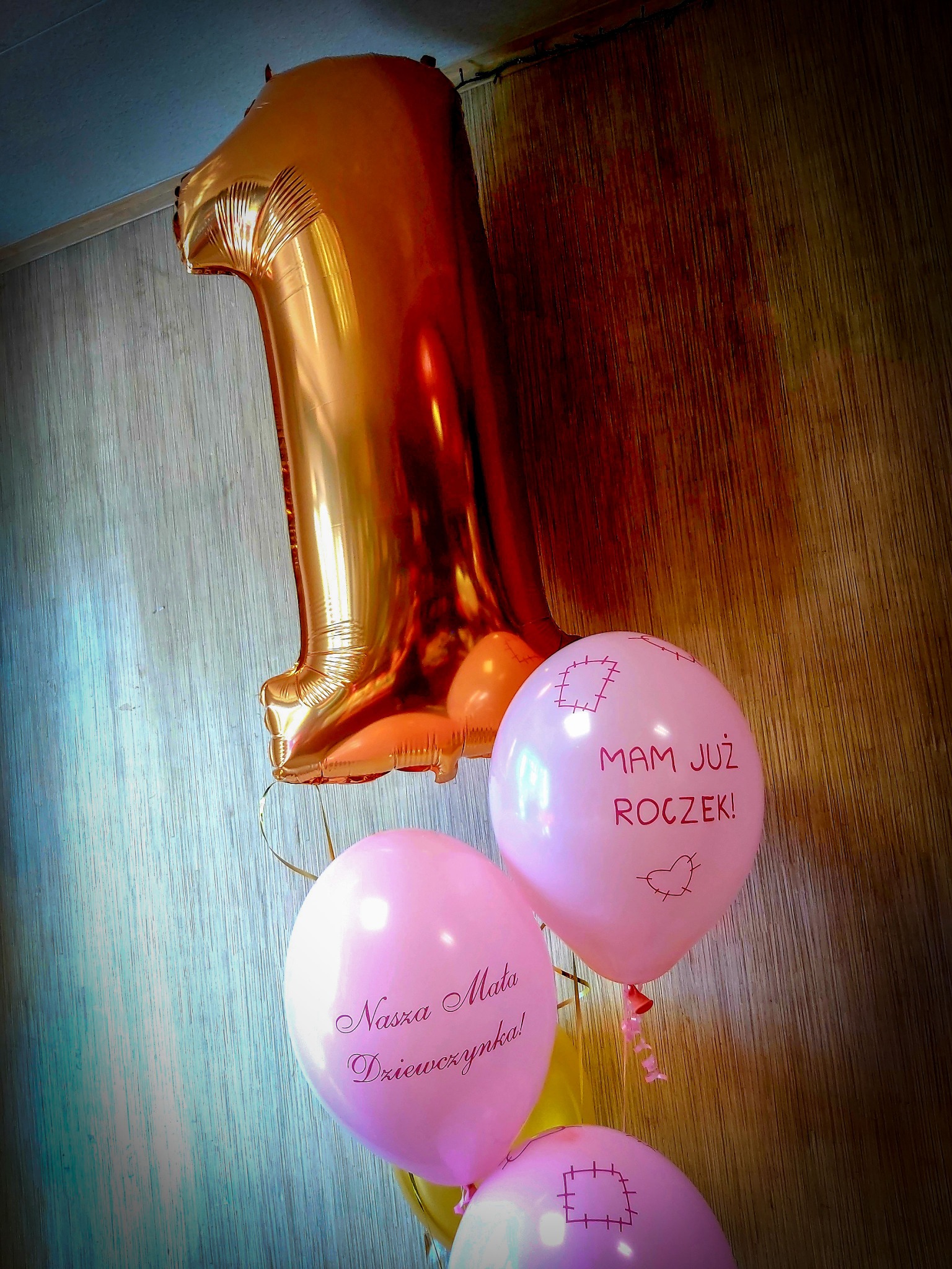 Zestaw balonów: duży, złoty balon w kształcie cyfry 1 oraz różowe balony z napisami 'Mam już roczek!' i 'Nasza Mała Dziewczynka!'